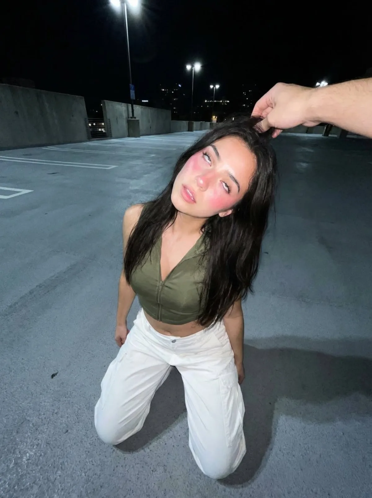 年轻女子跪在柏油路上，一只手从外部伸来
